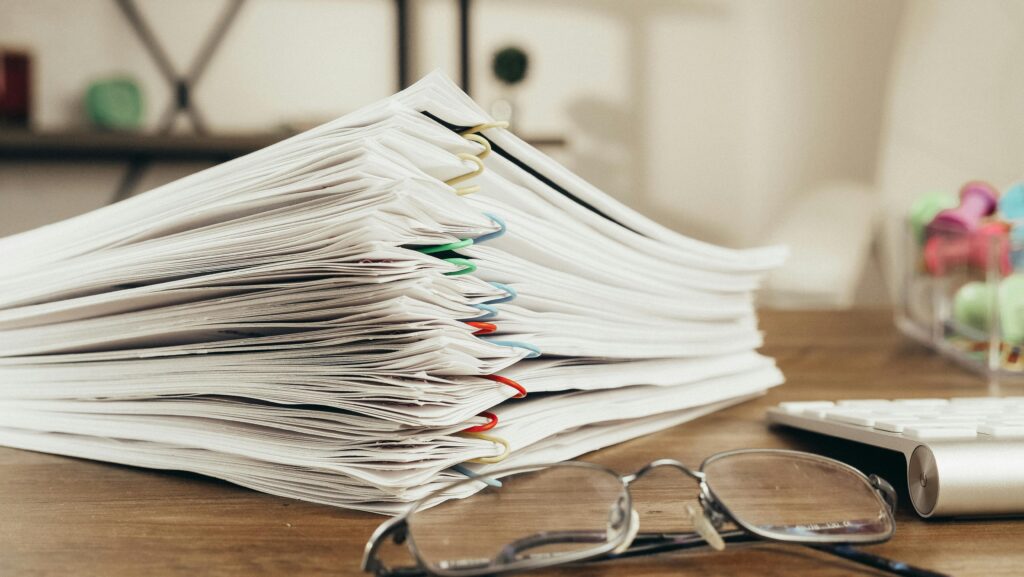 과태료 '폭탄' 부과 위기, 행정청의 법리적 오류 짚어내 처분 원천 차단 Close-up of a stack of office papers on a desk with glasses, emphasizing organization.
